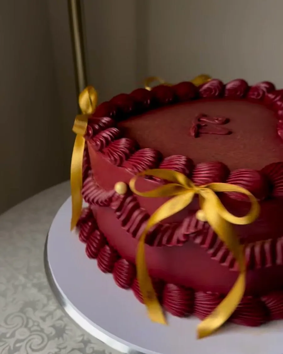 A deep maroon buttercream cake with a piped heart panel and gold satin ribbons